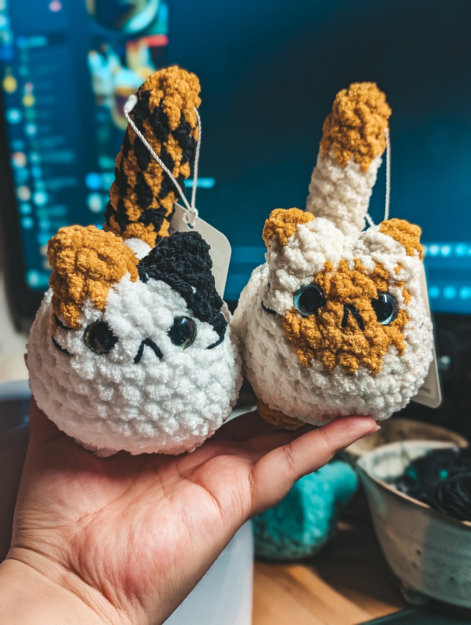 Two small custom crochet cat toys held in a hand with a blurred background